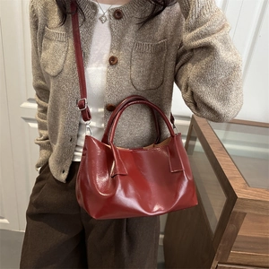 Minimalist burgundy bucket bag in glossy leather worn by a model with a shoulder strap