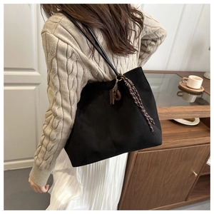 Detail showing a black suede tote bag with woven pendant on a model in beige sweater