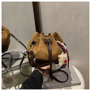 Detail of a brown suede bucket bag featuring a teddy bear charm and woven tassels