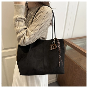 Detail of black suede tote bag with wooden knot charm and striped woven rope accessory