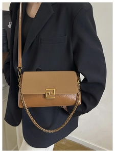 Detail of tan crossbody bag featuring textured leather, gold chain, and geometric buckle