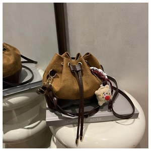 Detail of suede bucket bag with decorative woven charms and plush bear pendant