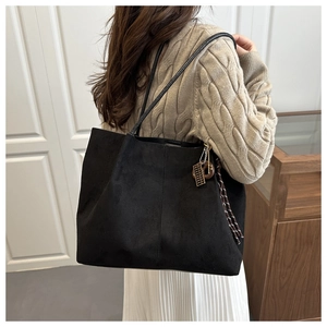 Detail of black suede tote bag featuring a metal brand tag and woven tassel charm
