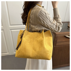 Detail of a large yellow tote bag with brown leather tassels and key pendant