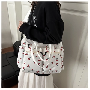 Detail of white canvas tote bag with red cherry print and multiple zipper pockets