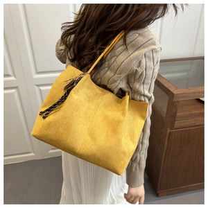Side view of large yellow suede tote bag with woven tassel detail on a shoulder strap