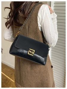 Detail of black leather shoulder bag with gold square buckle and chain strap on a model