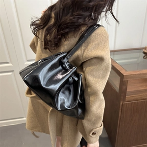 Glossy black patent leather pleated tote bag worn over the shoulder by a model