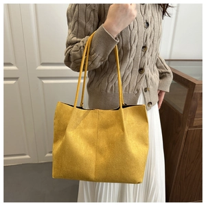 Detail of a bright yellow suede tote bag paired with a brown knit cardigan and white skirt