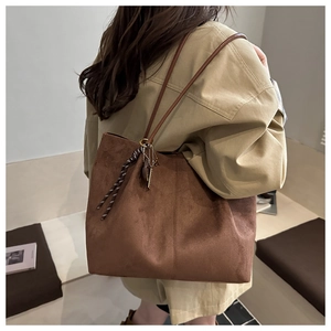 Detail view of large dark brown suede tote bag with decorative tassel and shoulder straps