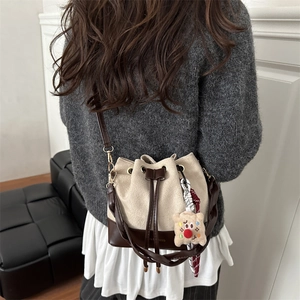 Minimalist drawstring bucket bag with contrast leather base and plush pendant