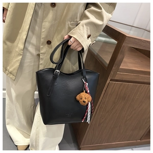 Détail d'un cabas noir en cuir avec un pendentif chien en peluche et boucle métallique