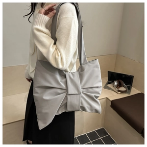 Graue übergroße Schultertasche in Schleifenform aus Nylon, getragen von einem Modell