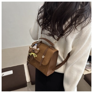 Close-up of brown vintage crossbody bag with flap cover and cute plush bear charm