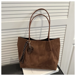 Close-up of deep brown suede tote bag featuring braided tassel and metal charm details