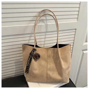 Detail of camel suede tote bag with woven tassel charm and slim straps on a white background