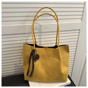 Close-up of yellow suede tote bag with woven charm detail on white shutter background