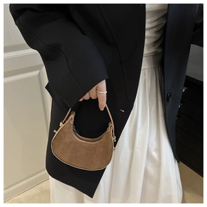 Chic brown suede and leather half-moon bag held by a model in a minimalist outfit