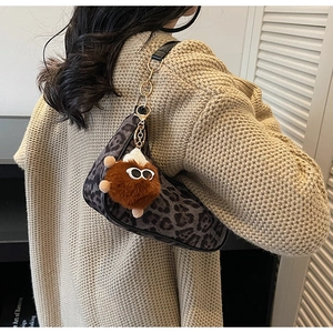 Dettaglio borsa a sella leopardata con ciondolo peluche e maglione beige a trecce