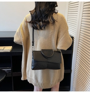 Detail of black faux crocodile leather handbag with metal round handle on beige sweater
