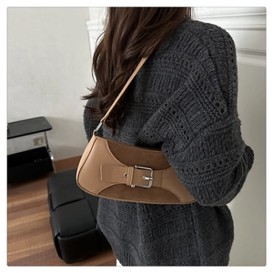 Primer plano de un bolso baguette camel con hebilla metálica y un jersey de punto gris