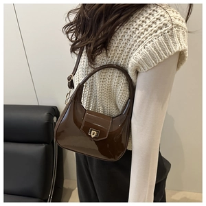 Side view of a brown glossy patent leather dumpling bag with gold buckle on a model