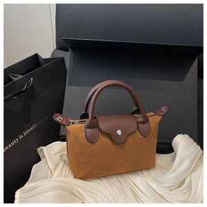 Close-up of brown suede mini handbag with leather strap on white silk background