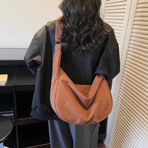 Brown leather moon tote bag with wide strap worn by a model in a minimalist home setting