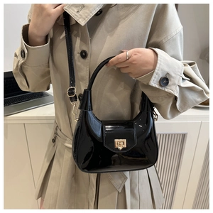 Glossy black patent leather handbag with gold buckle shown in an urban office setting