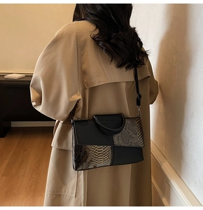 Detail of a chic shoulder bag featuring snake-print leather stitching on a minimalist model
