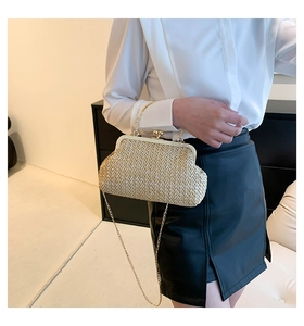 Detail der gewebten Stroh-Clutch mit Goldrahmen und Kette an einem stylischen Model