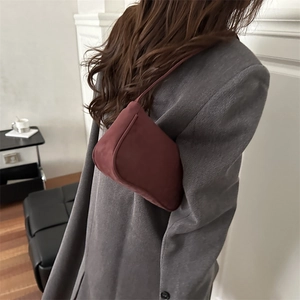 Elegante weinrote Wildleder-Achseltasche mit schlichtem Schultergurt auf grauem Mantel