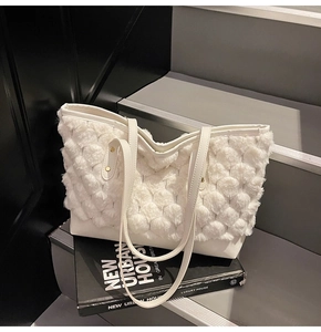 Détail d'un cabas blanc en peluche avec pompons et rivets dorés sur un escalier gris