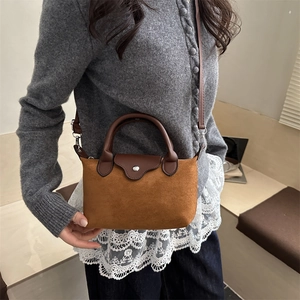 Minimalist brown suede crossbody bag with leather handles shown in a lifestyle setting