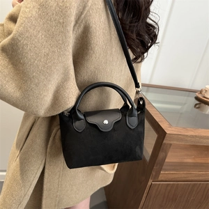 Minimalist black mini dumpling bag with round handles and crossbody strap on brown coat