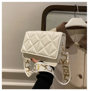 Detail of white quilted crossbody bag featuring a wide embroidered fabric shoulder strap