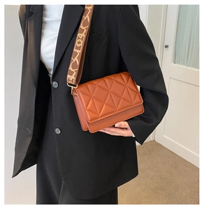 Brown quilted crossbody bag with stylish wide patterned strap shown on a black blazer