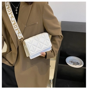 Detail of white quilted crossbody bag with stylish wide printed shoulder strap on a model