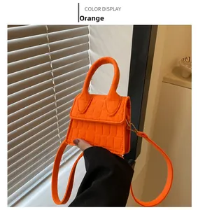 Detail van een feloranje mini crossbodytas met krokodillentextuur en goudkleurig metaal