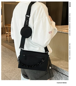 Detail of black crossbody bag with adjustable wide strap and round coin pouch charm