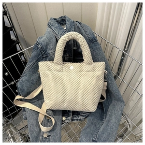 Detalle del bolso tipo cubo de pana crema con textura de burbujas y correa tejida