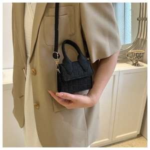 Model draagt een zwarte mini crossbody tas met gewatteerde textuur en gouden details