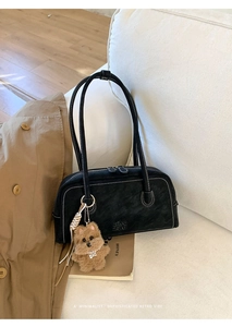 Détail du sac Boston en cuir noir avec surpiqûres blanches et charm ours sur un canapé