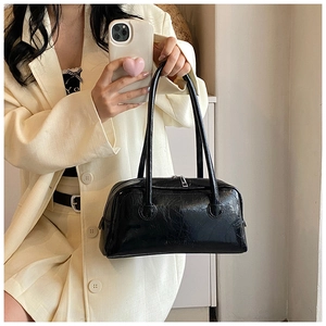 Detail of glossy black leather baguette bag showing long straps and zipper closure