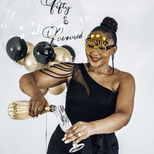 Golden Hello Fifty party glasses with black bead dress and festive balloon background