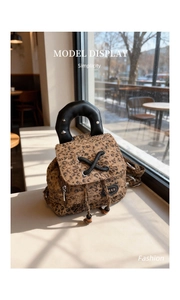 Detail showing leopard print backpack texture with leather handle and silver metal rivets