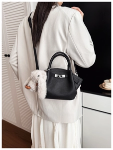 Detail of black litchi leather bucket bag with silver lock and plush rabbit charm