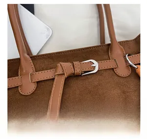 Detail of brown suede tote bag featuring slim leather strap and silver buckle closure