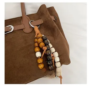 Detail of brown suede tote bag featuring retro beaded charm and leather trim accents