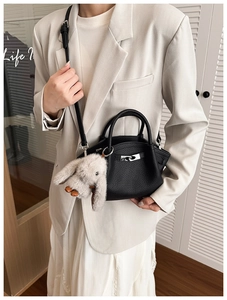 Detail of black pebbled leather bucket bag with silver lock and plush rabbit charm